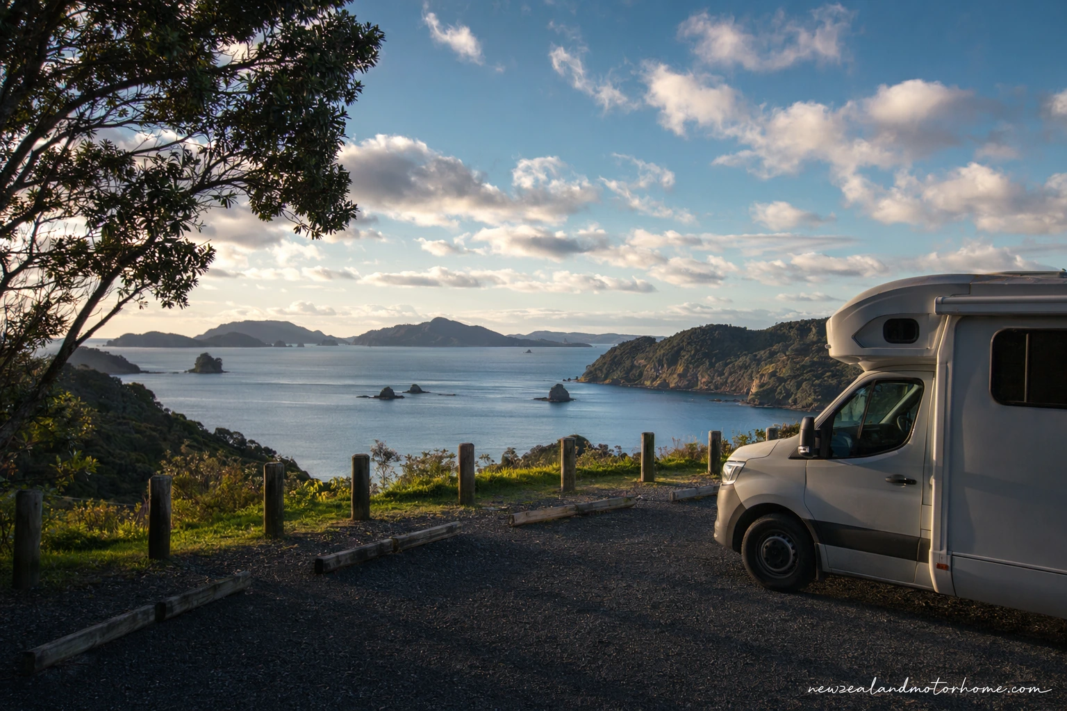 Campervan parked near the waterfront in the Bay of Islands with calm harbour water and green headlands