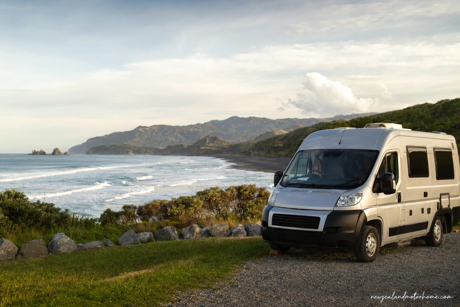 Campervan parked near a wild West Coast beach with rainforest and mountains in the distance