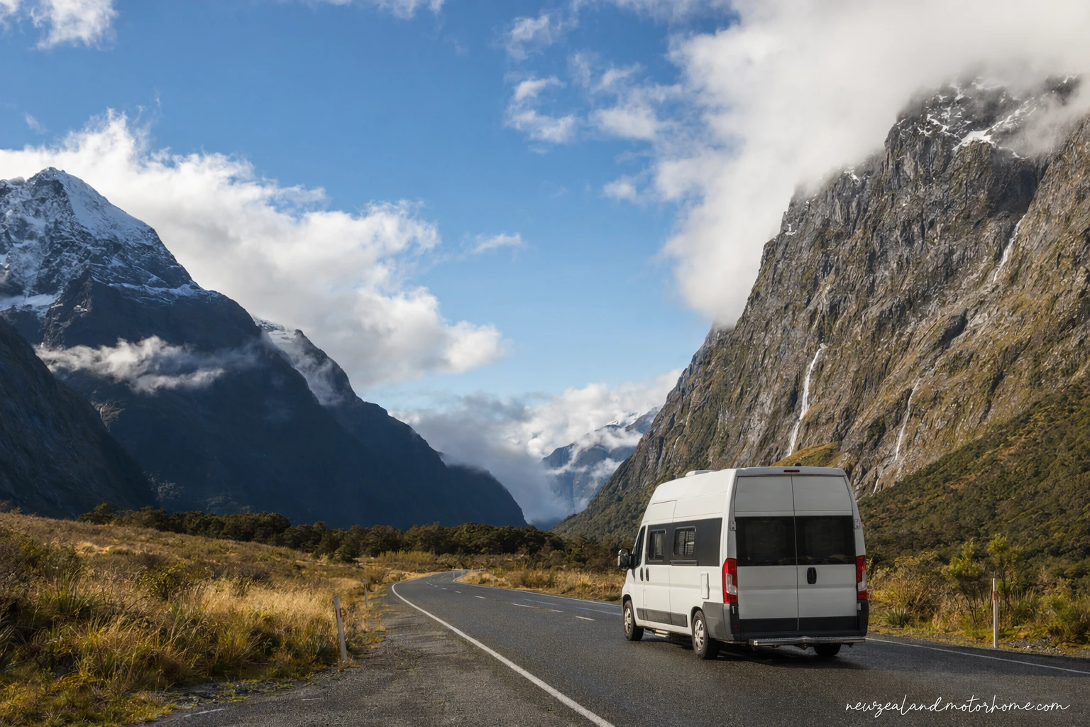 Campervan parked beside Milford Road in Fiordland with mountains and native bush ahead