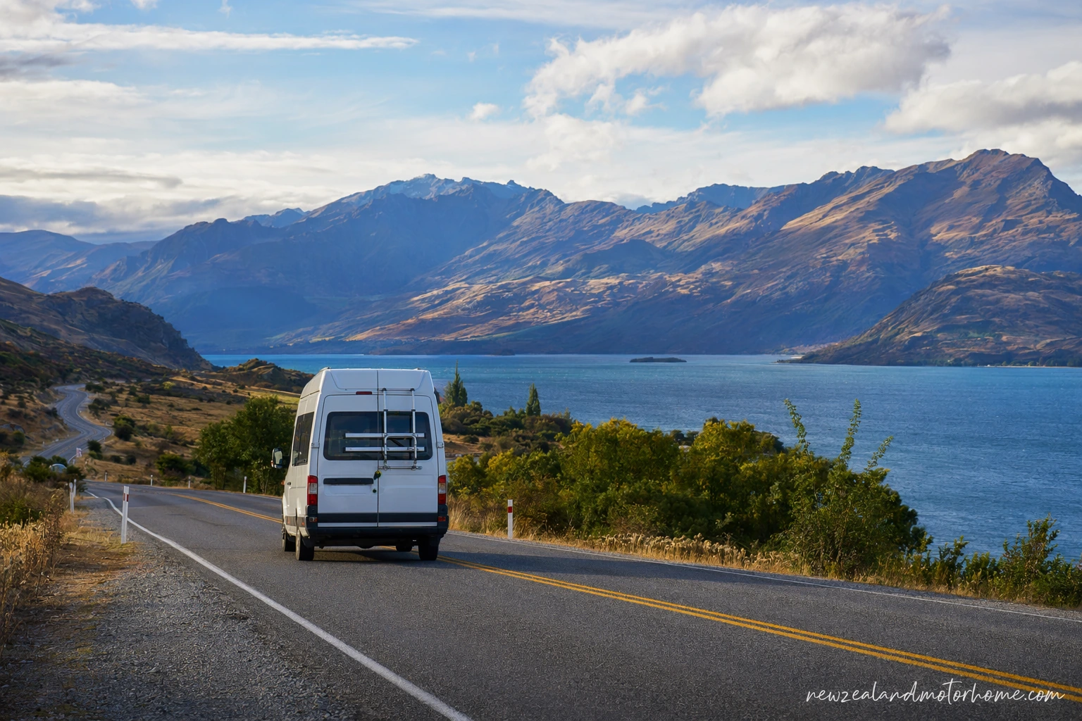 Campervan parked near Lake Wanaka with mountains behind and a clear lakeside road ahead