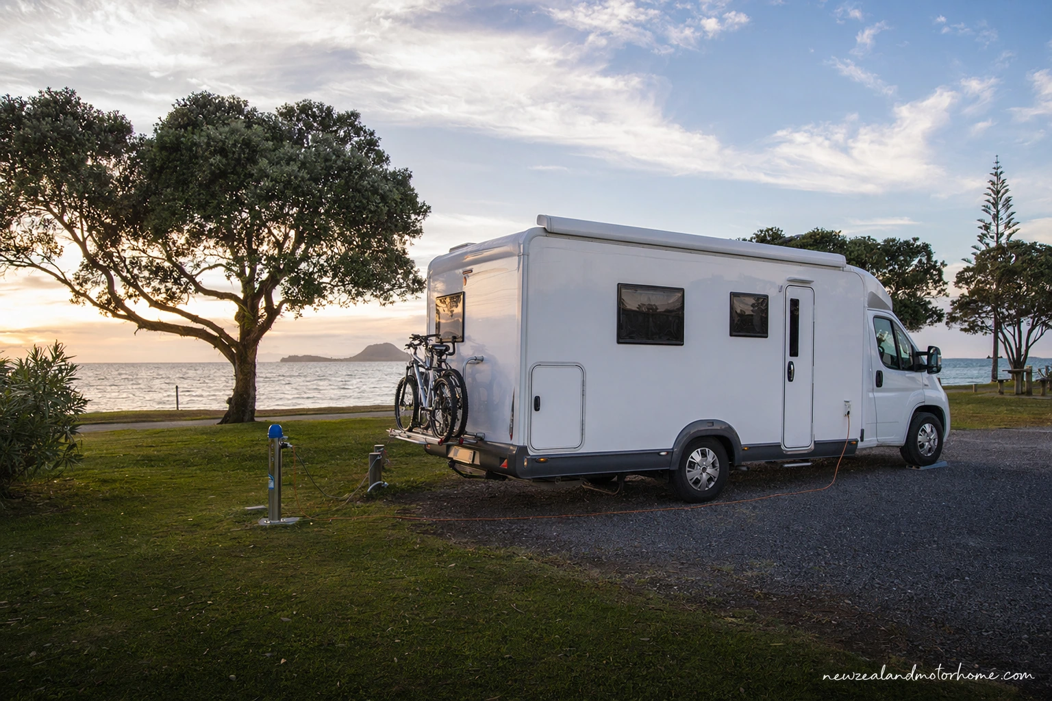 Campervan parked near the beach in Tauranga with harbour and coastal hills nearby