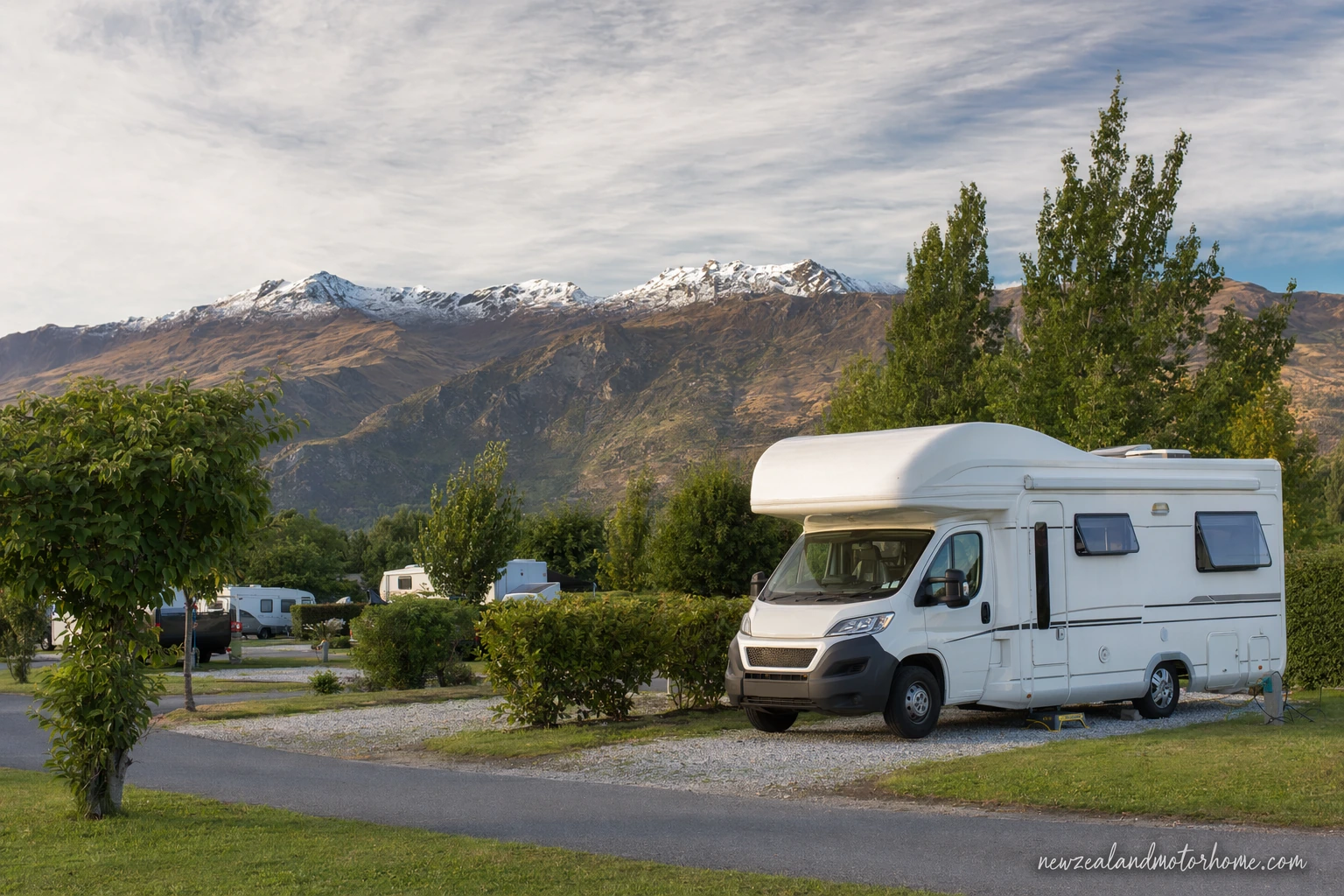 Campervan parked near Lake Wanaka with mountains behind and holiday park pitches nearby