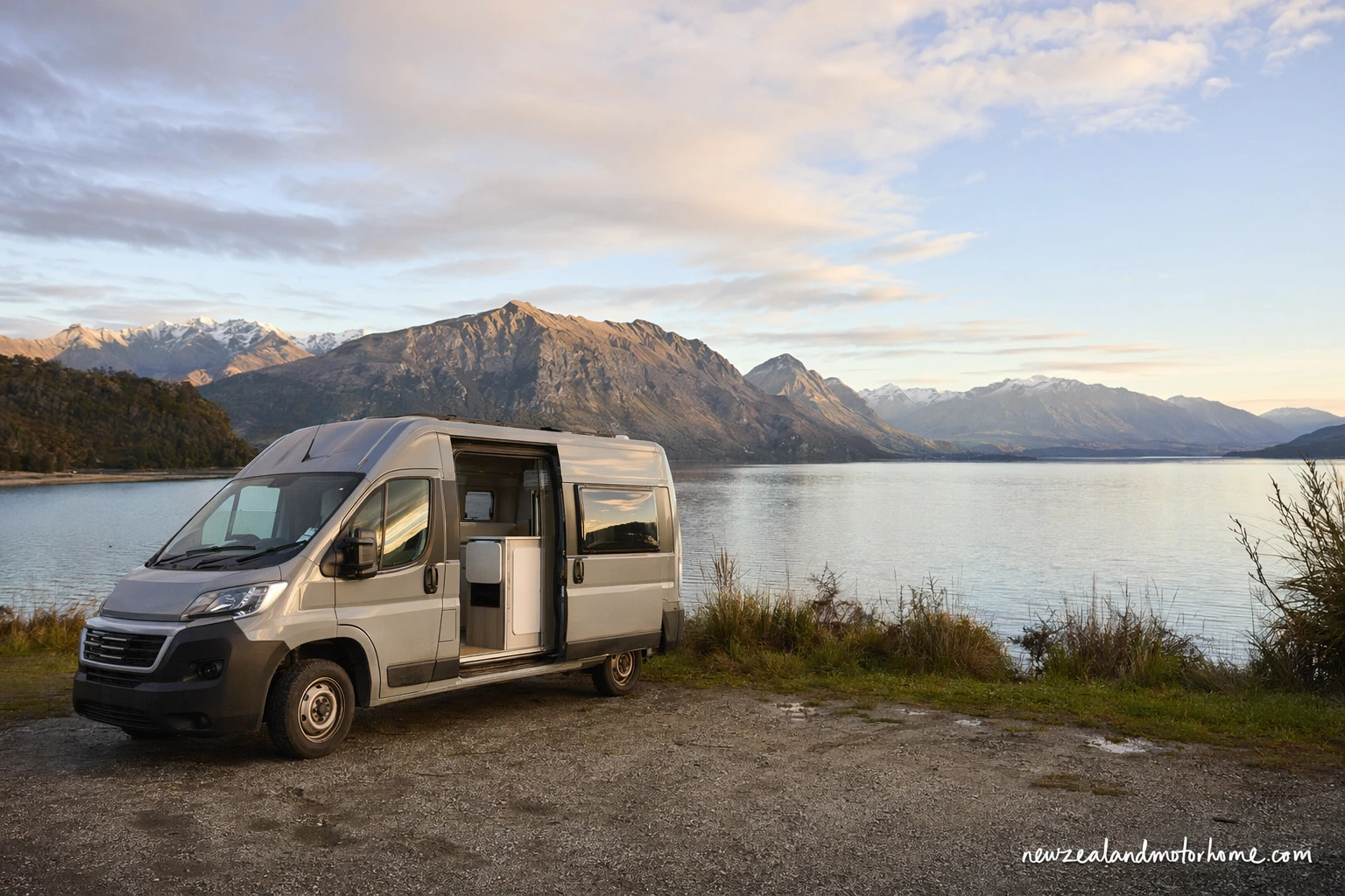 Compact campervan parked beside a quiet New Zealand lakeside campsite with mountains in the background