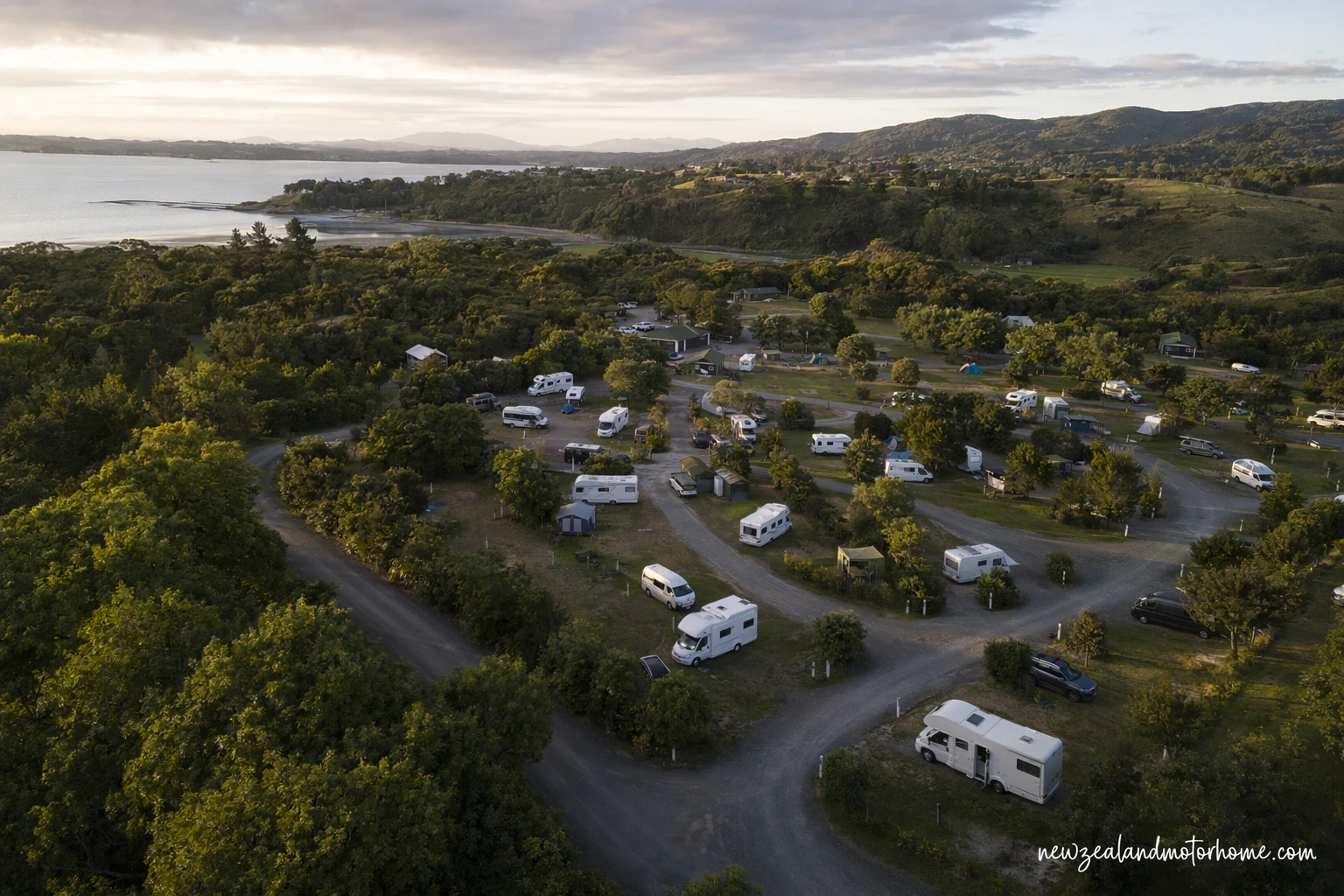 Campervan parked at a New Zealand holiday park with mountain views, grass sites and shared facilities nearby